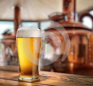 Chilled glass of light beer on wooden table and blurred copper brewing system at the background