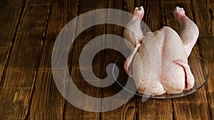 Chilled plucked chicken in a transparent plate on a rustic natural pine board