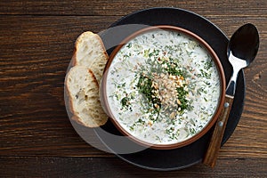 Chilled tarator with bread and spoon on wooden table ready to eat.