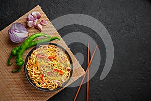 Chilli Garlic Hakka Noodles in black bowl on dark slate table top. Indo-Chinese vegetarian cuisine dish
