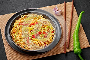 Chilli Garlic Hakka Noodles in black bowl on dark slate table top. Indo-Chinese vegetarian cuisine dish