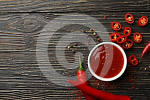 Chilli pepper and bowl sauce on wooden background, top view