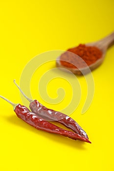 Chilli powder in wooden spoon with dry red chilly on yellow background