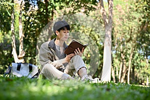 Chilling and focused young Asian male college student reading a book in the park