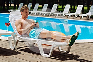 Prosperous businessman chilling while sunbathing near pool