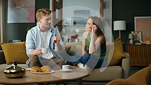 Chilling spouses drinking tea at sofa interior. Couple enjoying coffee talking