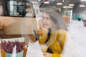 Chilling time in winter time of enjoyed young woman in window of comfortable cafe on street. Drinking coffee, dreaming