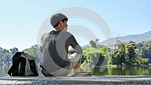 Chilling young Asian male college student relaxes sitting by the beautiful pond in campus park