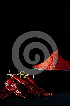 Chilly powder in black bowl with red chilly, dried chillies on black background