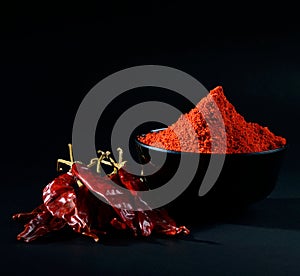 Chilly powder in black bowl with red chilly, dried chillies on black background