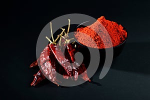 Chilly powder in black bowl with red chilly, dried chillies on black background