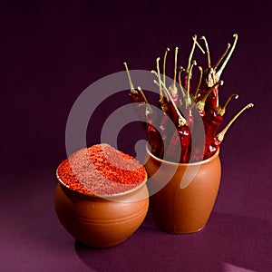 Chilly powder with red chilly in clay pots, dried chillies on dark background