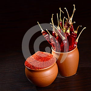 Chilly powder with red chilly in clay pots, dried chillies on dark background