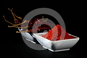 Chilly powder with red chilly in white plate, dried chillies on black background