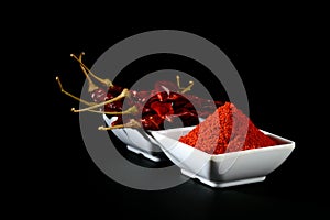 Chilly powder with red chilly in white plate, dried chillies on black background