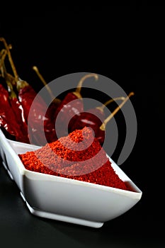 Chilly powder with red chilly in white plate, dried chillies on black background