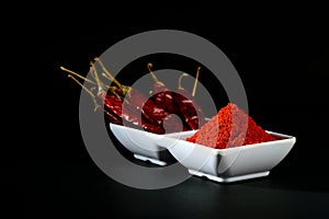 Chilly powder with red chilly in white plate, dried chillies on black background