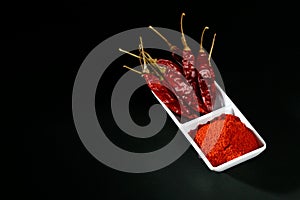 Chilly powder with red chilly in white plate, dried chillies on black background