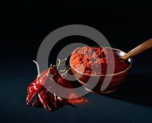 Chilly powder in wooden bowl with red chilly, dried chillies on black background