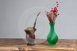 Chimarrao cuia next to a flower vase on top of a wooden table