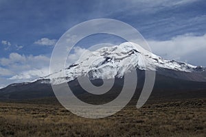 Chimborazo mountain tops covered in snow and surrounded with clouds under the blue sky in Ecuador