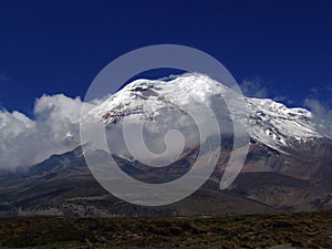 Chimborazo mountain tops covered in snow and surrounded with clouds under the blue sky in Ecuador