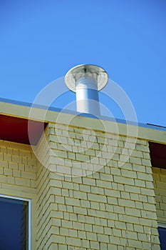 Chimney with metal vent on flat roof on side of building with wooden pannel or slat exterior walls in late afternoon