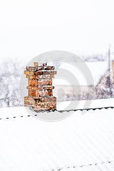 Chimney in red bricks with white snow on roof.