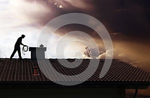 A chimney sweep cleans the chimney on a house roof while thunderclouds gather