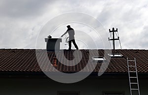 A chimney sweep cleans the chimney on a house roof photo