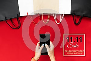China 11.11 single day sale concept, woman hand holding smartphone with shopping bag