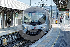 Fast metro train arrives at open-air station, people walk on platform. MTR Corporation.