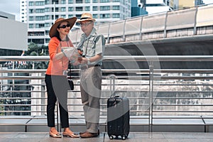 Chinese asian senior tourist couple with luggage and with map on hands having sightseeing tour in city of Bangkok