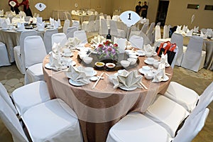 A chinese banquet table setting at a restaurant with white chairs and light pink table