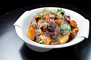 Chinese beef stew with young potatoes in sweet sauce, in white plate on black background