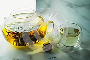 Chinese blooming tea. A glass teapot with a blooming tea flower on a white table. a cup of Chinese blooming tea and tea balls.