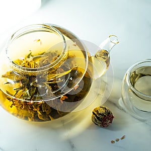 Chinese blooming tea. A glass teapot with a blooming tea flower on a white table. a cup of Chinese blooming tea and tea balls.