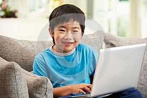 Chinese Boy Using Laptop Sitting On Sofa At Home