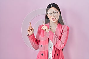 Chinese business young woman wearing glasses smiling and looking at the camera pointing with two hands and fingers to the side