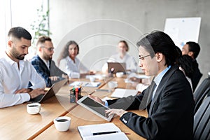 Chinese Businessman Using Digital Tablet During Corporate Meeting In Office