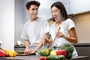 Chinese Couple Cooking Food And Laughing In Kitchen At Home