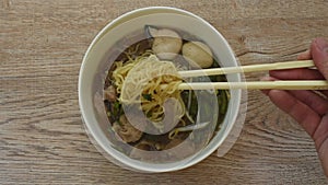 Chinese egg noodles topping braised pork and meatball in brown soup picking bt chopsticks on bowl