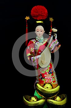 Chinese female doll in colourful costume with traditional gold ingots