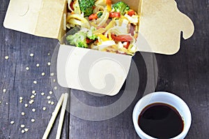 Chinese food, Noodles with pork and vegetables in take-out box on wooden table