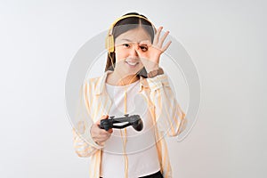 Chinese gamer woman playing video game using headphones over isolated white background with happy face smiling doing ok sign with