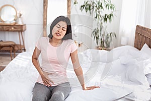 Chinese Girl Having Lower Abdominal Pain Sitting In Bed Indoors