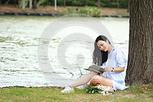 Chinese Girl reading a book under tree. Blonde beautiful young woman with book sit on the grass.