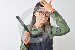 Chinese hairdresser woman wearing glasses holding comb over isolated white background stressed with hand on head, shocked with