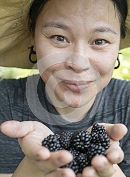 Chinese happy woman portrait with blackberries in open palms.