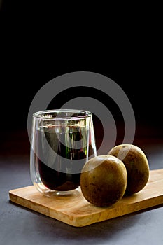 Chinese herb juice concept. Arhat fruit juice in a glass with arhat fruit on a wooden chopping board on black background